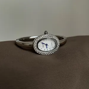 Detailansicht einer eleganten ovalen Armbanduhr mit Kristallen und blauen Zeigern