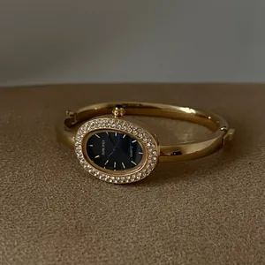 Elegante goldene Armreif-Uhr in ovaler Form mit funkelnder Strass-Lünette und dunklem Zifferblatt