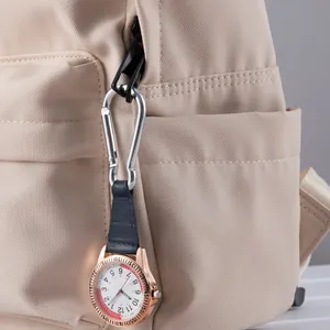 Detailopname van een roségouden carabiner horloge met blauwe leren band aan een beige rugzak