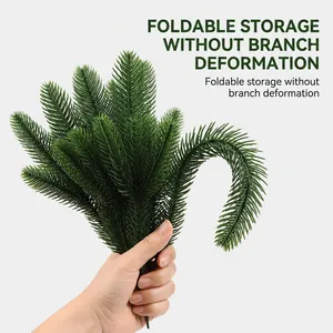 Detail view of flexible green artificial pine branches being held by a person's hand.