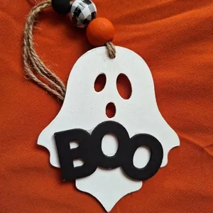 Detail view of a cute white wooden ghost ornament featuring black BOO text and beads.
