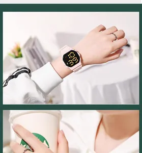 Close-up of a pink LED digital sports watch worn on a wrist in a cozy cafe setting.