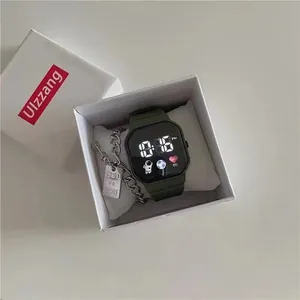 Detail of a dark green digital watch and a silver chain bracelet in a minimalist box.
