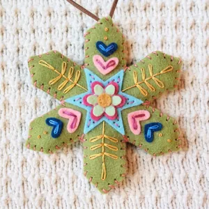 Detailed view of hand-embroidered green felt snowflake ornament with colorful motifs.