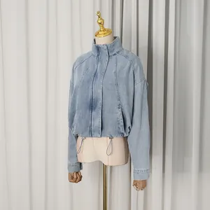 Detail shot of a light blue oversized denim jacket with a high collar and drawstring hem.