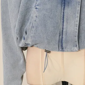 Close-up detail of a casual light blue denim jacket featuring a metal toggle hem