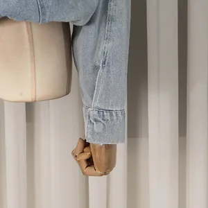 Close-up detail of a light blue denim jacket cuff showing fine stitching on mannequin