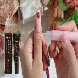 Applying Nymixa air-dry nail glue to attach a red flower ornament on a manicure.