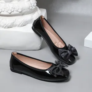 Detail view of black patent leather ballet flats with large fabric bow decoration.