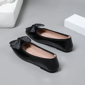 Elegant black patent leather ballet flats featuring grey satin bow detail from a side view