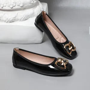 Close-up of black patent leather ballet flats with decorative gold interlocking heart buckle