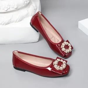 Close-up of elegant red patent leather ballet flats with pearl circle buckle decoration.