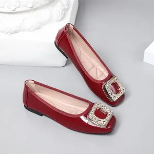 Detail shot of red patent leather flats with rhinestone square buckle on square toe.