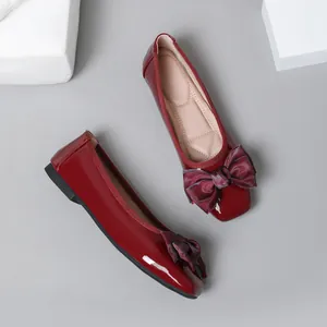 Top-down view of glossy burgundy patent leather ballet flats featuring large decorative bows