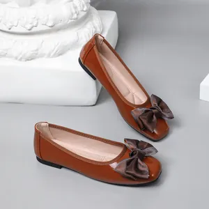 Close-up detail of brown patent leather ballet flats featuring an elegant satin bow