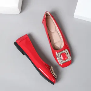 Close-up detail of red patent leather flat shoes with a decorative rhinestone buckle.