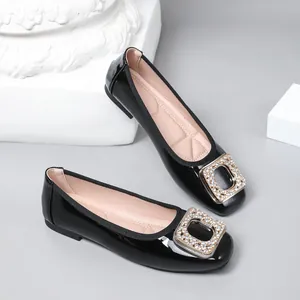 Detailed close-up of black patent leather flats with an elegant rhinestone square buckle.