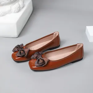 Close-up of brown patent leather ballet flats with decorative bow and square toe design