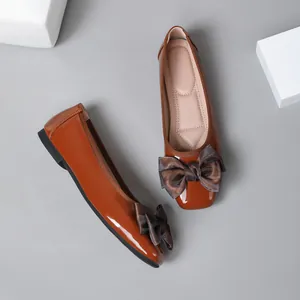 Detail of brown patent leather flat shoes with large elegant silk bow on the toe.