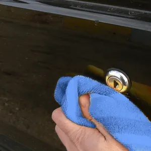 Nahaufnahme eines blauen Mikrofasertuchs, das eine glatte schwarze Autooberfläche reinigt.