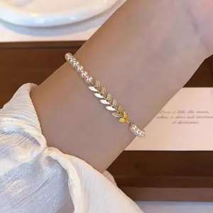Close-up detail of elegant pearl bracelet featuring a golden leaf charm on a woman's wrist
