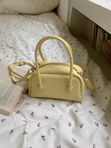 Dettaglio ravvicinato della borsa bauletto gialla su un letto a fiori minimalista