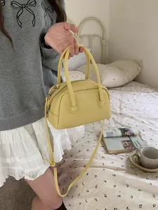 Borsa a mano a cuscino in ecopelle gialla tenuta da una modella in camera da letto