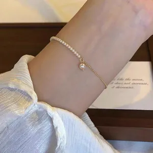 Close-up detail of an elegant gold chain bracelet with delicate white pearls worn on a wrist