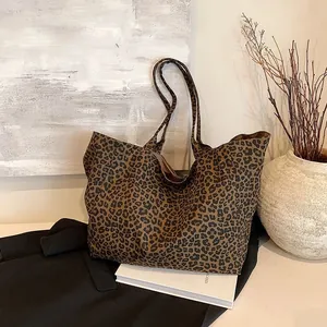 Large leopard print canvas tote bag shown in a cozy lifestyle setting with rustic decor.