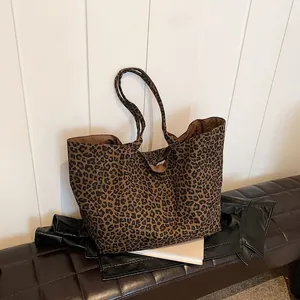 Detail view showing a large leopard print canvas tote bag resting on a dark leather bench.