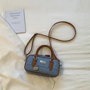 Chic denim bowling bag with brown leather handles and a lock charm on a soft background.