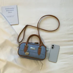 Detailed view of a blue denim Boston bag with brown leather handles and a lock charm.