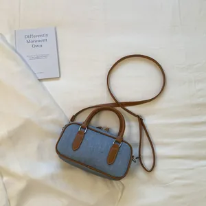 Elegant minimalist denim bowling bag with brown leather straps on a white textured background.