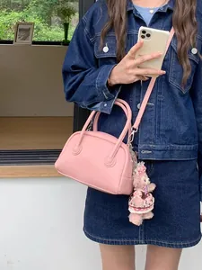 Dettaglio di una borsa a cuscino in pelle rosa con ciondolo di peluche e tracolla