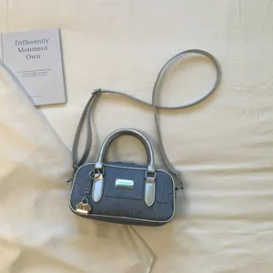 Macro detail of a stylish denim bowling bag featuring silver handles and a long strap