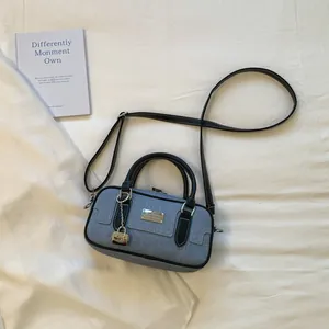 Detail view of a blue denim bowling handbag with black handles and silver logo plaque