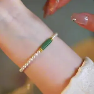 Elegant pearl bracelet detail featuring a central green cylindrical gemstone on the wrist