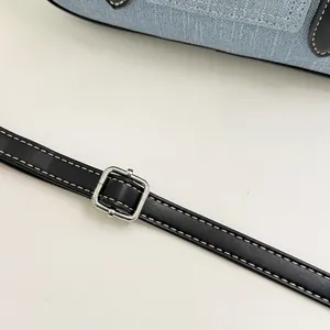 Detailed macro view of black leather adjustable shoulder strap and silver buckle on denim bag