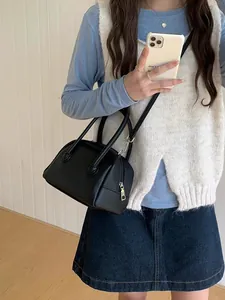 Dettaglio di una borsa a bauletto in pelle nera a grana portata a tracolla per l'uso quotidiano.