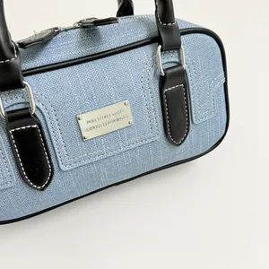 Close-up of light blue denim bowling bag with black leather handles and silver hardware