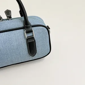 Close-up of a blue denim bowling bag featuring black leather trim and fine stitching detail
