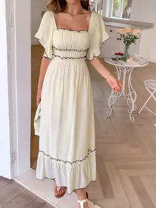 Detail view of cream summer dress with black ruffled edges in a cozy interior setting.