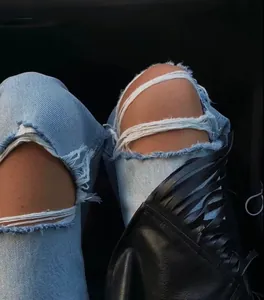 Detailed close-up showing heavy distressed ripped knee design on light blue denim jeans