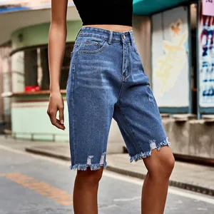 Macro view of high-waisted distressed denim bermuda shorts with frayed hems and ripped accents.