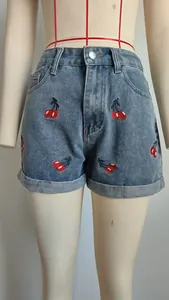 Detailopname van gewassen blauwe spijkershorts met levendige rode kersenborduurwerk.