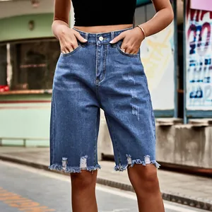 Close-up of blue distressed denim Bermuda shorts with trendy raw hem and ripped details.