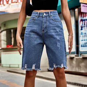 Detail shot of blue distressed denim Bermuda shorts with frayed hem and ripped accents.