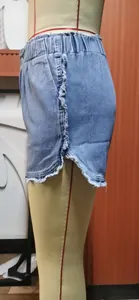 Side detail of blue denim shorts with frayed edges and elastic bubble waistband