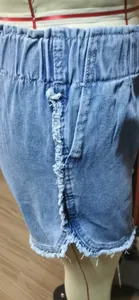 Detailed view of blue denim shorts with frayed edges and elastic paperbag waist.