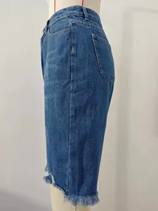 Side view of blue distressed denim Bermuda shorts with raw fringe hem on mannequin.
